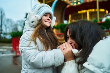 Genç kız bir panayırda annesiyle sevgiyle konuşurken gülümsüyor..