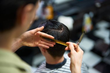 Bir berber, yoğun bir berber dükkanında bir tarak ve makas kullanarak müşterinin saçını budardı..