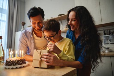 Ebeveynler mutlu bir şekilde bakarken bir çocuk heyecanla hediyeyi açar..
