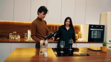 Bir çift, şık mutfaklarında sıcak bir anı paylaşıyor, kırmızı şarap dolduruyor ve birlikte gülüyorlar..