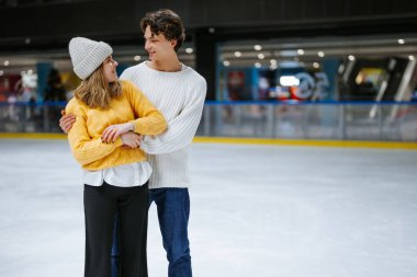 Genç çift buz pateni pistinde güler ve kucaklaşır..