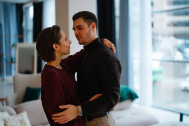 İki birey kucaklaşır, şık bir iç mekanda birbirlerinin gözlerine bakarlar..