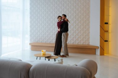 Bir çift şık, minimalist ve doğal ışıkla dolu bir odada sıcacık kucaklaşıyor..