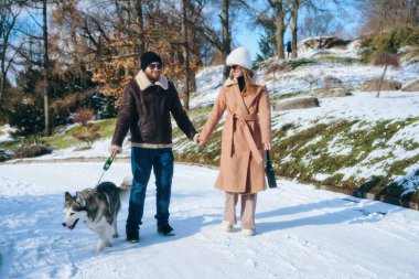 Erkek ve kadın, karlı bir ortamda köpeklerini gezdirirken el ele tutuşuyorlar..