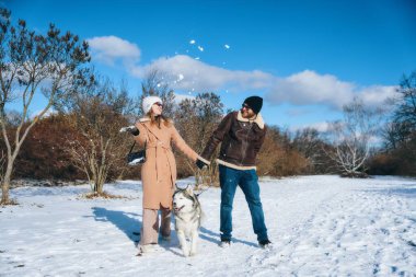 Mutlu çift bir köpekle kış gezintisi sırasında havaya kar fırlatıyor..