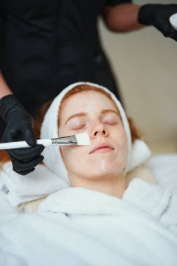 Bir kadın rahatça yatarken rahatlatıcı bir yüz tedavisinden zevk alır..