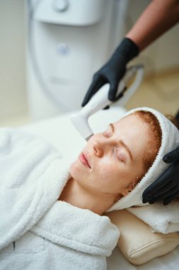 Kaplıcadaki kadın sabahlık giyerken yüz bakımı görüyor..