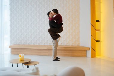 İki birey, şık bir yaşam alanında dururken sevgi dolu bir kucaklaşmayı paylaşıyor..