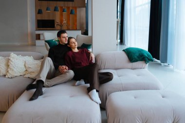 Çift, modern bir yaşam alanında yumuşak bir kanepede birlikte vakit geçirmenin keyfini çıkarıyor.
