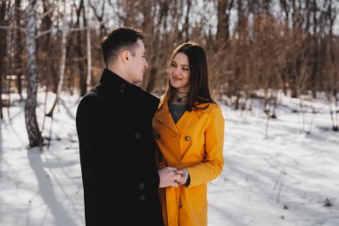 Genç çift, karlı bir arazide yürürken el ele tutuşup gülümsüyor..