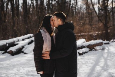 Karla kaplı ağaçlarla çevrili iki insan sarılıp öpüşüyor..