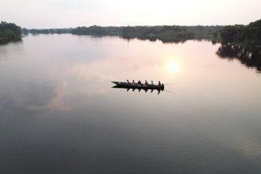Güneş batarken sakin bir nehirde altı kişi yol alır..