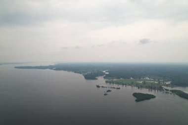 Hava perspektifi bulutlu bir gökyüzünün altında yeşillikle çevrili bir nehri gösteriyor.