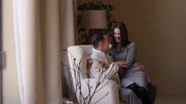 Gülümseyen bir çift, sıcak bir odada otururken samimi bir kahkaha atar..