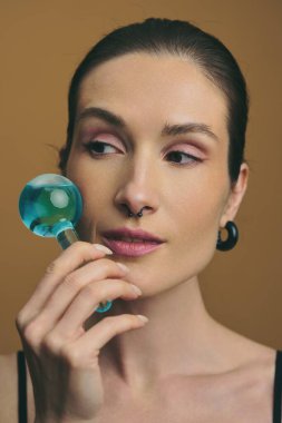 Kadın model nazikçe yanağına mavi bir masaj aleti bastırıyor..