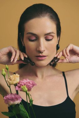 Model çiçek saplarını tutarken sakin bir ifade sergiler.