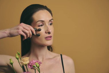 Model taze çiçekleri sıcak renklerde tutarken yüz silindirleri uygular.