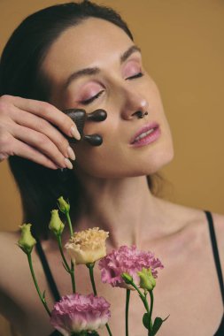 Kadın renkli çiçeklerle çevriliyken yüz aletleri kullanıyor.