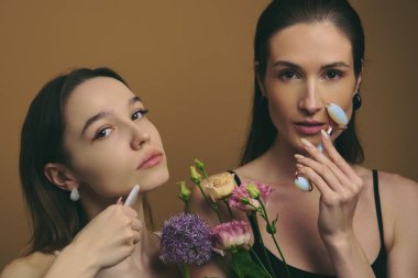 Kadınlar evde çiçek tutarken cilt bakımına girerler.