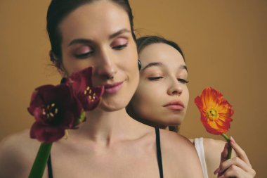 İki kadın renkli çiçeklerle poz veriyor, gösterişli güzellik ve dostluk..