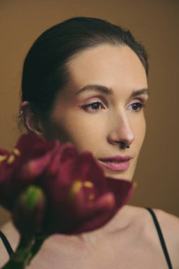 Keskin bakışları olan biri, koyu bir çiçeği sıkıca tutarken düşünceli bir şekilde bakar..