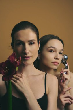 İki kadın yan yana durur, biri elinde bir çiçek, diğeri ise bir güzellik aleti tutarak..