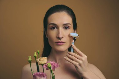 Bir kadın yüzüne taze çiçeklerle çevrili bir yeşim taşı takıyor..