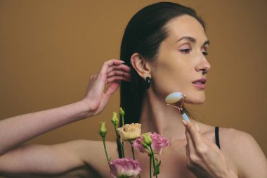 Bir kadın çiçekleri nazikçe tutarken yüzüne yeşim bir silindir sürer..