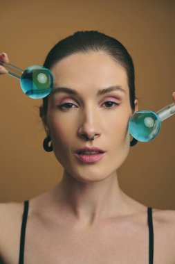 Genç bir kadın stüdyoda güzelliğini göstermek için mavi sıvı şişeler kullanır..