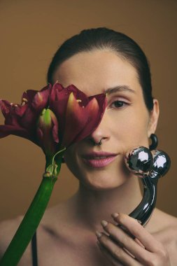 Stüdyoda elinde çiçek ve yüz silindiri tutarken gülümseyen bir kadın..