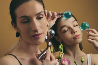 İki insan yüz gereçleri ve çiçeklerle cilt bakımı yapar..