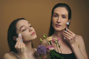 İki kadın cilt bakımı yapıyor, ürünler ve çiçekler sergileniyor..