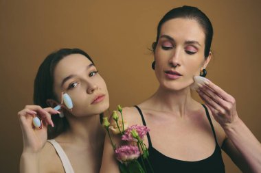 İki kadın aletlerle cilt bakımı yapıyor ve taze çiçekleri bir arada tutuyorlar..