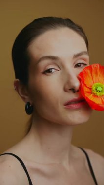 Manken yüzüne çarpıcı bir çiçekle zarif bir poz veriyor, güzelliği vurguluyor..