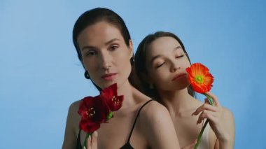Bu klipte iki kadın zarif poz verirken canlı çiçekler tutuyor..