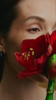 Bir insan güzel kırmızı bir çiçeği nazikçe yüzünde tutar, sakinliğini gösterir..