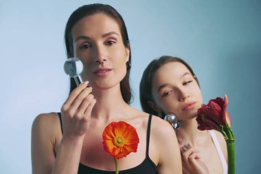 İki kadın ellerinde çiçekler ve cam objelerle yaratıcı ifadeler sergiliyor..