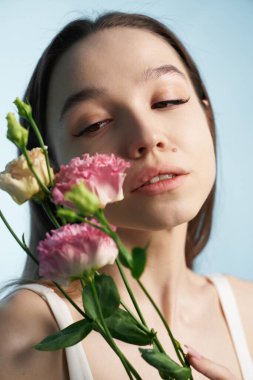 Güzel poz verirken çiçek tutan sakin bir yüzü olan genç kadın..