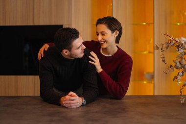 Gülümseyen çift, sıcak bir mutfak ortamında sevgi dolu bir şekilde etkileşime girer..