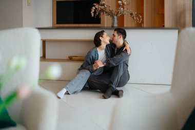 Bir çift birey, sıcak bir odada yerde otururken keyifli bir anı paylaşıyor..