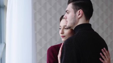 Sevgi dolu bir çift birbirine yakın durur, dışarı bakarken huzurlu bir anı paylaşırlar..