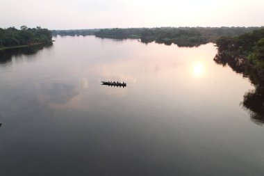 Kürekçiler, akşam gökyüzünü yansıtan sakin bir nehirde yol alırlar..