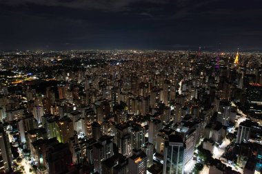 Geceleri aydınlatılan engin bir şehirde sayısız bina ve ışık sergileniyor..