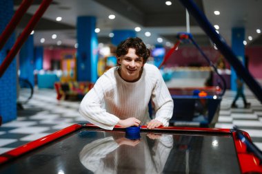 Gülümseyen genç adam renkli bir oyun salonunda hokey oynuyor..