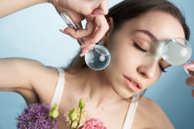 Kadın, renkli çiçekleri, büyüteçle, yumuşak arkaplana karşı inceliyor..