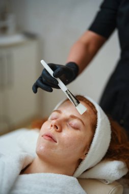 Maske takan bir kadın güzellik uzmanı ile yüz bakımı görüyor..