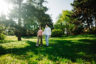 İki insan güneş ışığıyla dolu canlı yeşil bir parkta sakin bir şekilde yürümekten zevk alır..