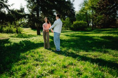 Güneş ışığıyla dolu yemyeşil bir parkta iki kişi neşeyle birbirine bağlanıyor..