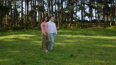 Güneşli bir günde uzun ağaçlar ve yeşilliklerle çevrili bir çift el ele yürür..