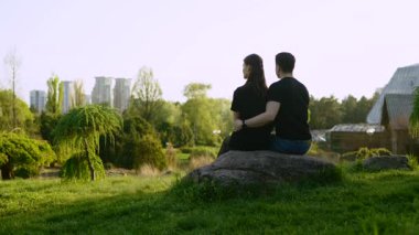 Aşıklar birlikte bir kayanın üzerinde oturur, doğanın sessiz güzelliğinin tadını çıkarırlar..